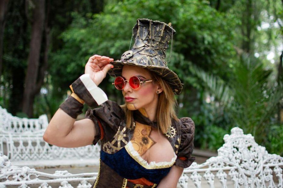 Woman in red steampunk corset and black top hat with gears posing in a park