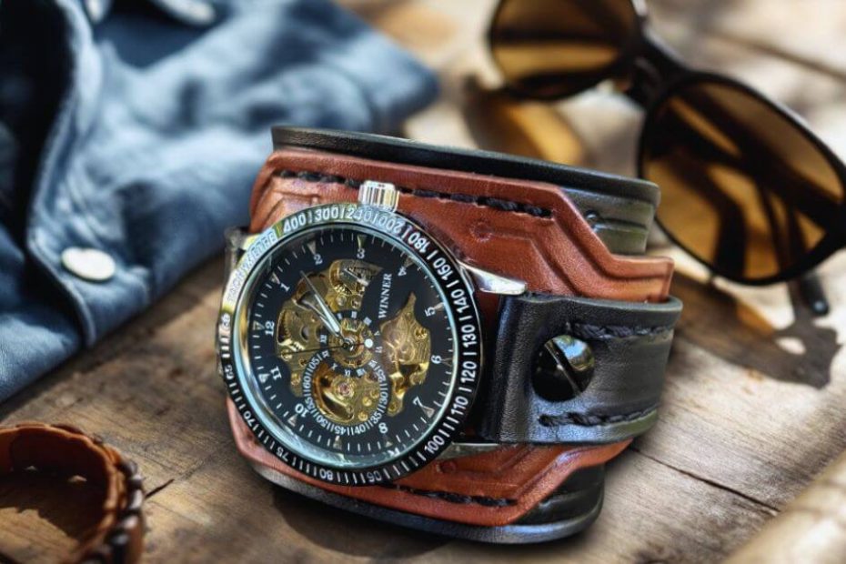 Handcrafted leather cuff watch styled with sunglasses and denim jacket on rustic wood background.
